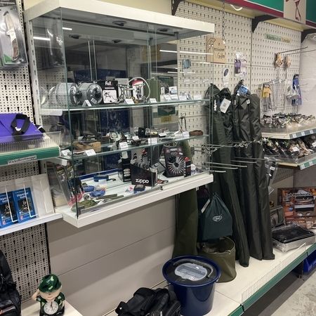 Verkaufsvitrine mit Zubehör und Markenartikeln, daneben Taschen, Kleidung und Anglerbedarf