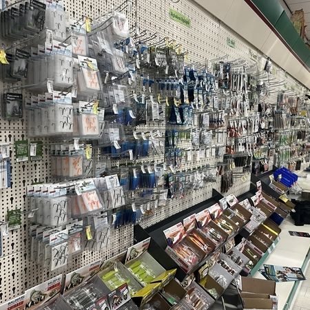 Wand voller Angelhaken, Blinker und Kunstköder in Einzelverpackungen mit Auslagefläche darunter
