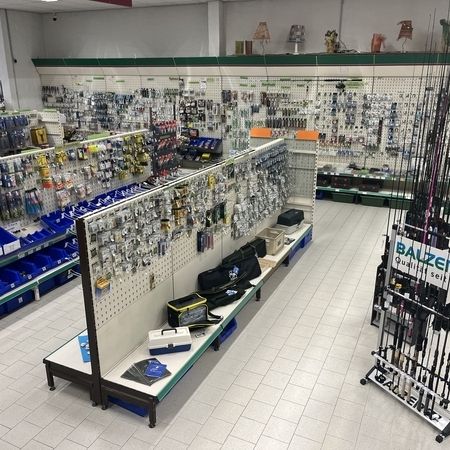 Blick über eine Verkaufsfläche mit Haken, Ködern und Zubehör für Angler an Wand und Mittelregal
